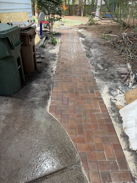 The same side yard with the brick walkway laid and edged, bare soil still open on both sides.